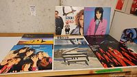Photo showing 7 vinyl records arranged upright and lying flat, featuring artists INXS, Joan Jett, Rolling Stones, Sting, Rod Stewart, and Supertramp plus one more, illustrating lot contents.