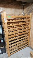 Single pine wine rack with multiple scalloped horizontal shelves for storing wine bottles in basement setting.