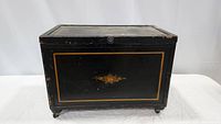 Front view of the black wooden cabinet chest showing floral decoration and gold trim on front panel.
