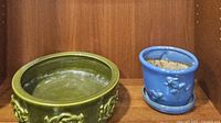 Photo showing large green ceramic planter with raised decorative knots and a smaller blue glazed planter beside it.