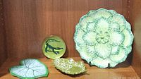 Photo showing the full set of decorative serving dishes, including various leaf-shaped ceramic plates, an enamel metal alligator plate, and terra cotta chip and dip set