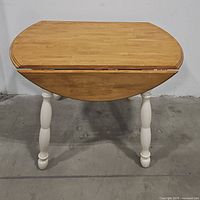 Front view of round wooden drop leaf table with closed leaves and painted turned legs.