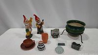 Two ceramic garden gnomes playing instruments, small pots, teacup planter, black and white patterned pot, bag of soil cover, decorative rocks, green elevated ceramic planter.