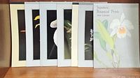 Seven Asian botanical and landscape prints displayed together, including the 1984 Japanese Botanical Prints calendar, showing partial close-ups of floral designs and varied background colors.