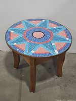 Front angled view of the round table showing the colorful mosaic tile top and wooden legs.
