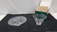 Two clear crystal dishes displayed on a black cloth, including a wider ribbed flower-shaped dish and a smaller fluted Noritake dish with box