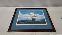 Full view of framed painting showing the ship and ocean scene with blue sky and clouds.