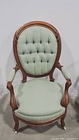 Front view of Victorian style armchair showing tufted oval backrest, cushioned seat, wooden frame and upholstered armrests.