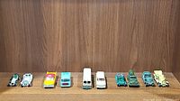 10 vintage diecast cars and vehicles displayed in a row on wooden shelf.