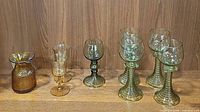 Wide view of all glassware showing the amber pitcher, two amber cordial glasses, and five green stemmed glasses in one image.