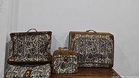 Three floral patterned vintage luggage pieces shown together, two garment suitcases and one smaller carrying bag.