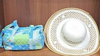 Photo showing a blue and green quilted patchwork handbag and two brimmed hats (one medium straw hat with open weave detail and one light wide brim straw hat)