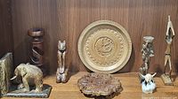 Display of various wooden carved pieces including spiral candleholder, animal figurines, fish plate, and carved wooden plaques