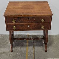Front view of table showing two drawers with brass ring pulls and lyre-style side supports