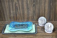 Two-toned rectangular serving tray outward facing with green center and dark brown border, blue trinket dish, abstract organic tray, and pair of carved ceramic candleholders on wood surface.