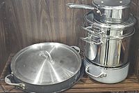 Stacked stainless steel pots including a lidded saut pan, sauce pan, steamer pot, and stock pot