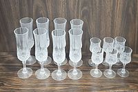 Full set photo showing 10 tall crystal glasses and 5 smaller glasses arranged in 2 rows on wooden surface against wood backdrop.
