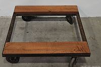 Top-down view of the wooden dolly cart showing the metal frame, wooden planks, and casters.