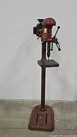 Full height view of the red metal Atlas drill press standing on a metal base showing the overall structure and height.