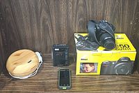Wide shot of all items shown together on shelf: Nikon D50 camera on its box, Panasonic stereo radio cassette recorder, SkyCaddie golf GPS, and InnoGear diffuser.
