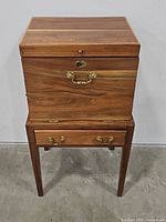 Front view of closed wooden chest on stand showing hinged lid and brass hardware