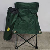 Front view of the green folding chair with the matching carry bag leaning against it.