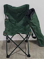 Front view of the green Masters folding chair with the carry bag leaning beside it.