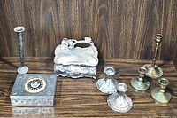 Photo showing all metal items in lot including vintage ornate jewelry box, rectangular metal box with sun motif, and six metal candleholders of various sizes and finishes
