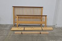 Headboard, footboard, wooden slats and one side rail displayed on floor against wall