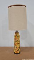 Full view of ceramic table lamp with vintage off-white fabric shade, showing the lamp's height and design.