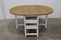Front view of a rustic folding table showing the round wood top and white painted folding legs.