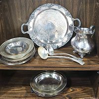 Overall view of shelf showing large round tray, pitcher, two ladles, small bowls, and bottom round tray