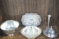 All five silver serving pieces arranged on wooden background: large bowl, smaller bowl, platter, covered butter dish, and small silver vase or candlestick holder