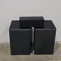 Pair of Yamaha speakers and an Optimus center speaker placed against a white wall on concrete floor