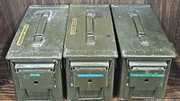 Three olive green military ammo boxes placed side by side, showing top handles and front labels reading 'EXPLOSIVE', 'MISC PAPERS', and 'IMPORTANT PAPERS'.