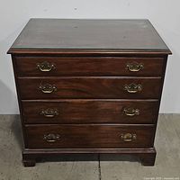 Front view of the vintage chest showing four drawers with brass handles and glass top.
