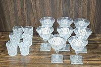 Front view of the 6 old fashioned glasses grouped together behind the 8 footed champagne glasses on a dark wood surface.