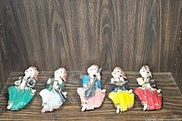 Five wooden musician figurines arranged in a row on a wood paneled shelf, showing different colors and instruments.