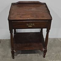 Front view of wooden side table with closed drawer and brass hardware handle.