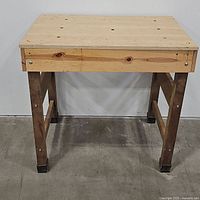 Front view of a wooden workbench showing a smooth top surface with holes and sturdy legs.