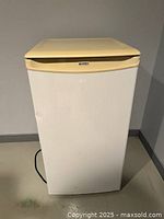 Front view of white mini bar fridge with beige top edge, showing small dent on front.