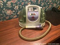 Front view of Bissell Little Green ProHeat rug cleaner with hose attached and turbo brush nozzle visible on wooden surface.