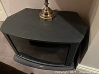 Top front angle of black wooden TV stand showing curved smoked glass door and smooth top surface with an object placed on top.