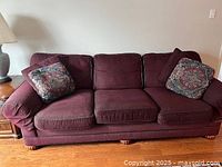 Front view of the burgundy sofa showing removable seat cushions and two throw cushions on the arms.