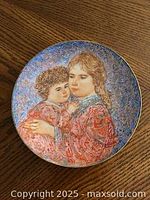 Front of a gold-edged collector plate depicting two children, a woman holding a child, in warm colors with detailed brushwork and a blue background.