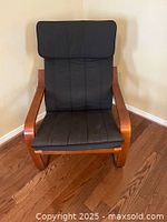 Front view of black padded chair with cushioned seat and headrest, wooden frame, sitting on hardwood floor.