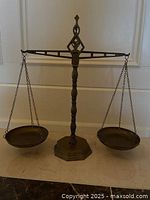 Front view of full decorative brass scale showing the balance beam with two hanging pans and octagonal base.
