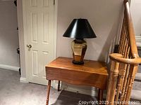 Wooden drop leaf dining table with two leaves, showing closed leaf on one side and lamp on top.