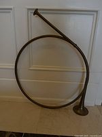 Front view of the vintage English hunting horn showing its circular coiled brass body and flared bell placed resting on floor against a wall.