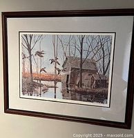 Full view of framed print depicting a rustic barn by water with ducks flying, surrounded by a wooden frame.